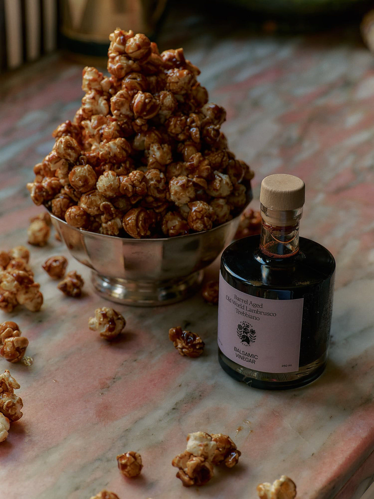 A metal bowl holds caramel popcorn beside a bottle labeled