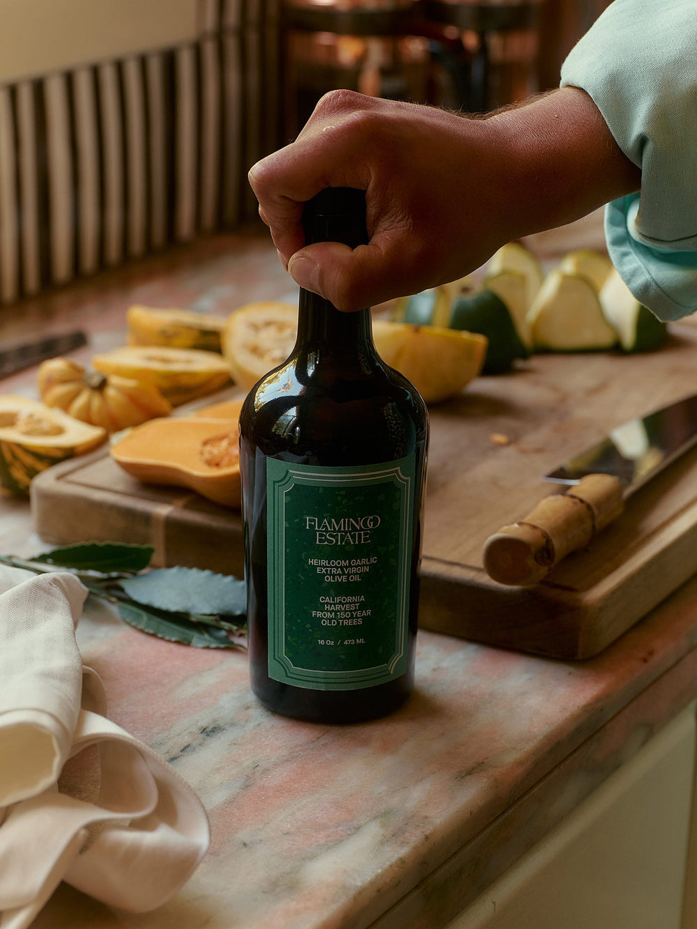 A chef’s hand holding Garlic Infused Olive Oil while preparing fresh ingredients.