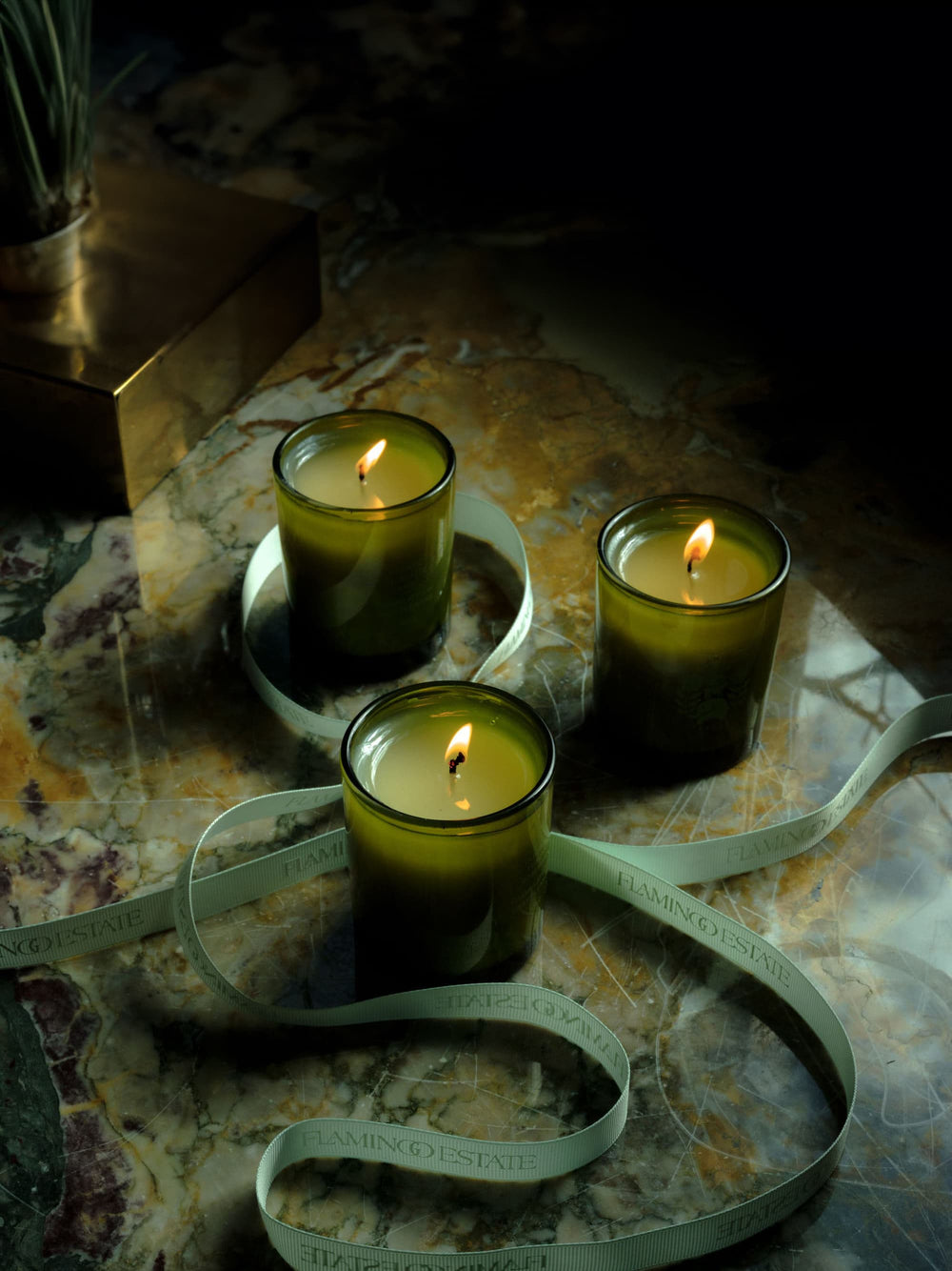 Three lit candles from the Mini Three Sister Set by Flamingo Estate, arranged on a marbled surface with a branded ribbon