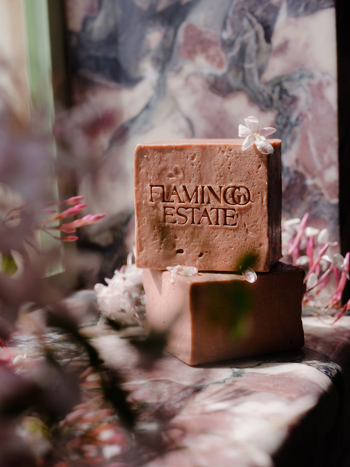 Two pink soap bars rest on a stone surface, adorned with small white flowers.