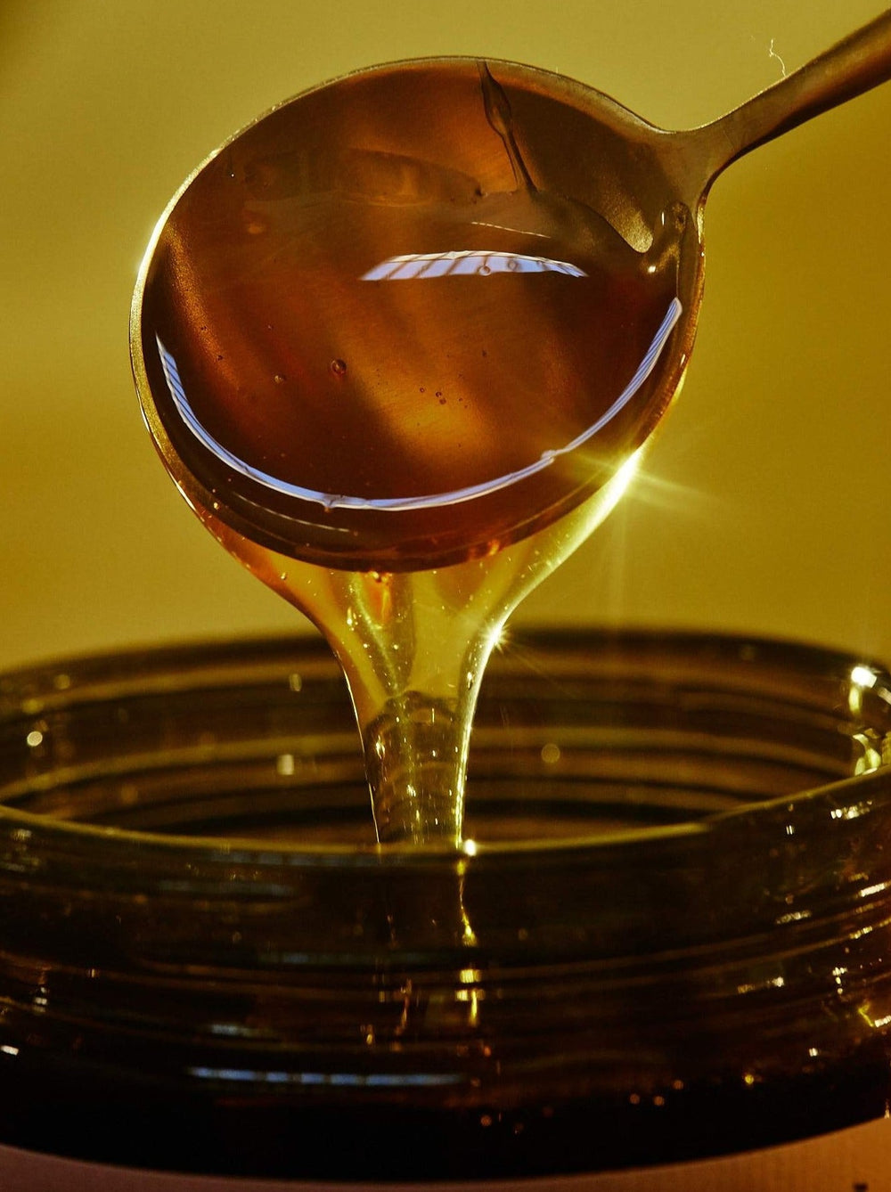 Round Gold Spoon Dripping Honey Into An Open Jar