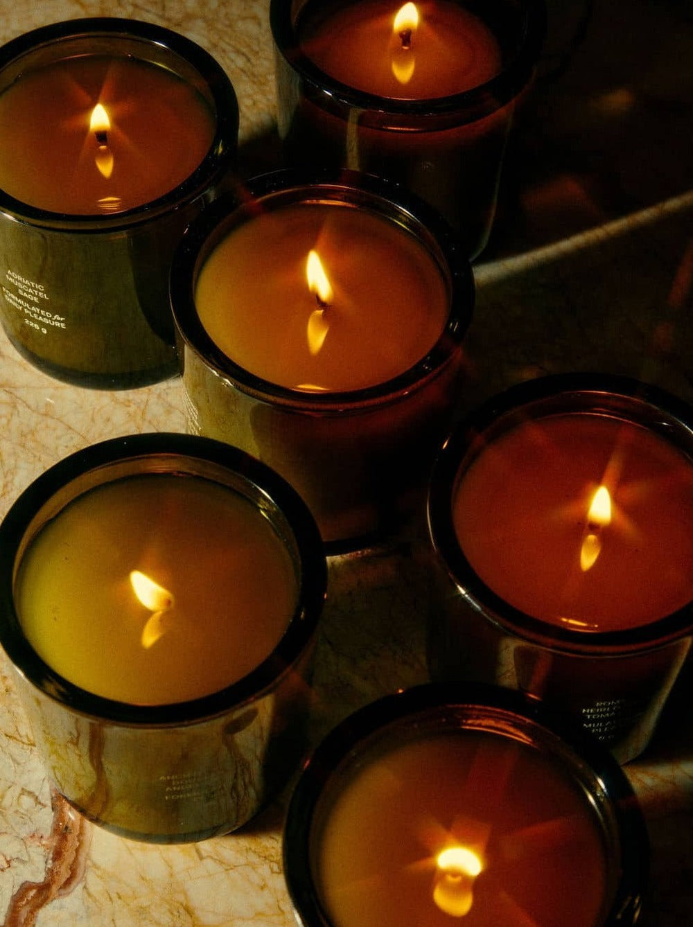 Candles flicker warmly, set in dark jars on a marbled surface.