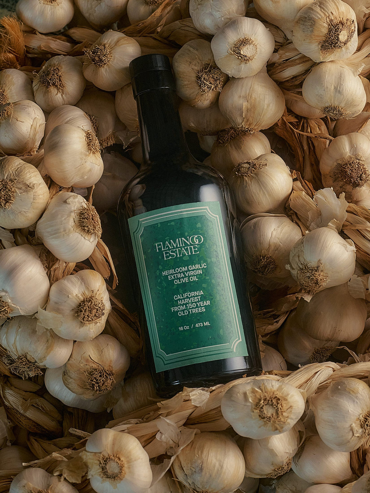 Garlic Infused Olive Oil bottle nestled among fresh garlic cloves.