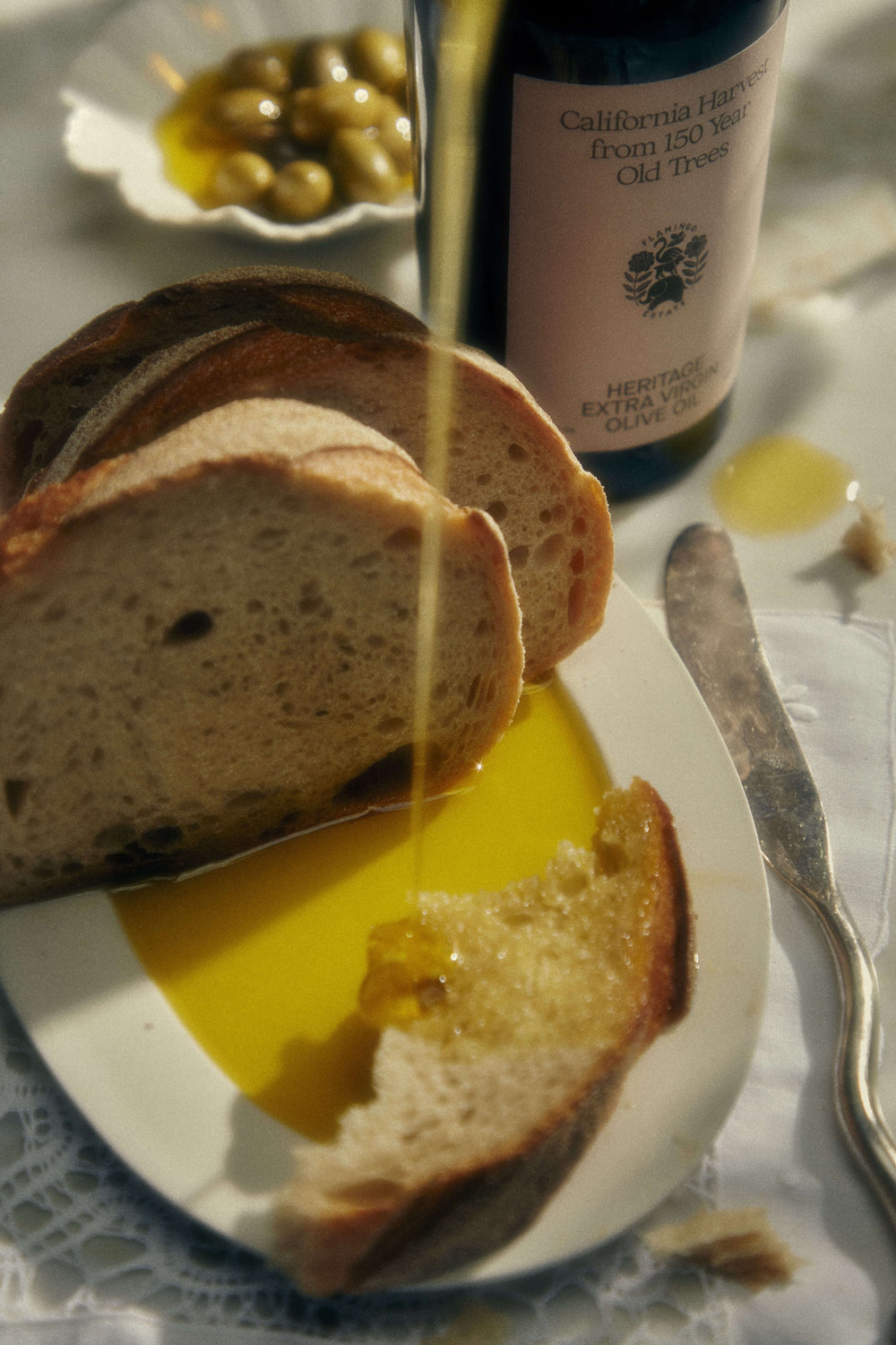Bread slices soak in olive oil on a white plate; nearby, a bottle labeled 