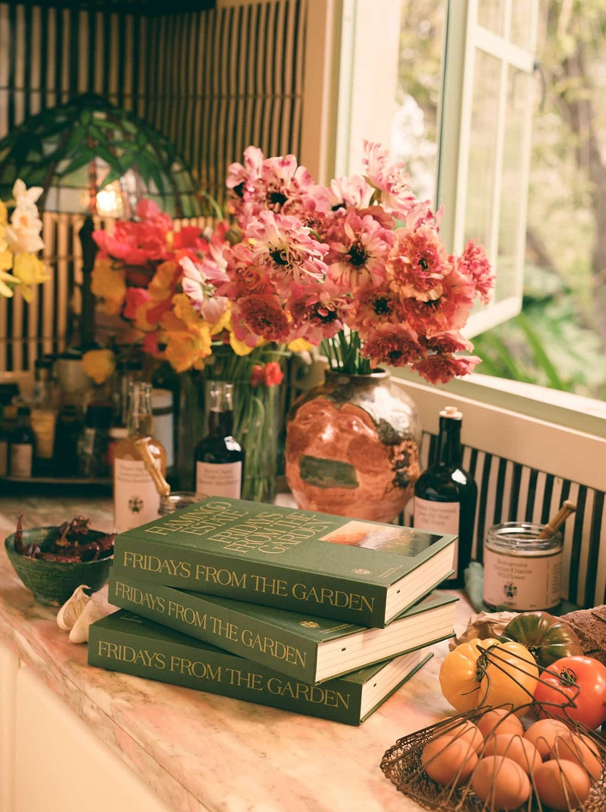 Books and a vase of pink and yellow flowers rest on a kitchen counter.
