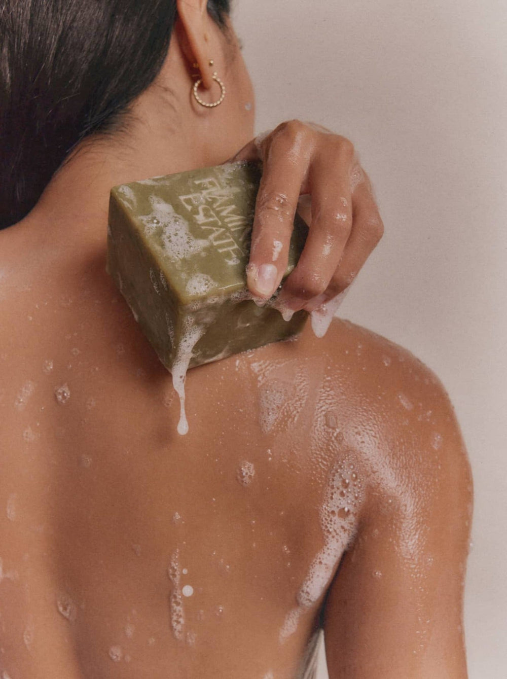 A hand scrubs a soapy back with a green block of soap.
