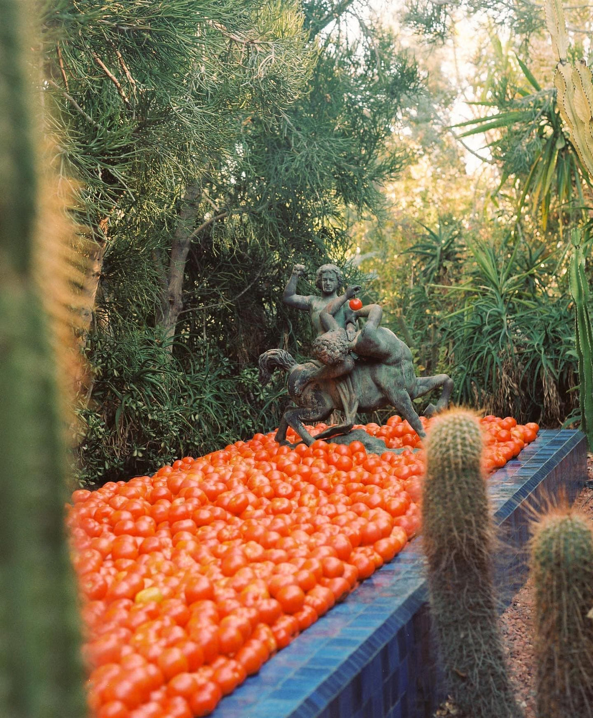 A sculpture of centaurs holds a tomato, surrounded by a large pile of tomatoes.